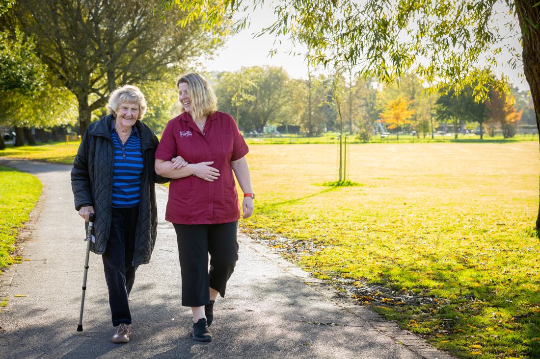 A carer walking with a client who uses a walking stick, in the park