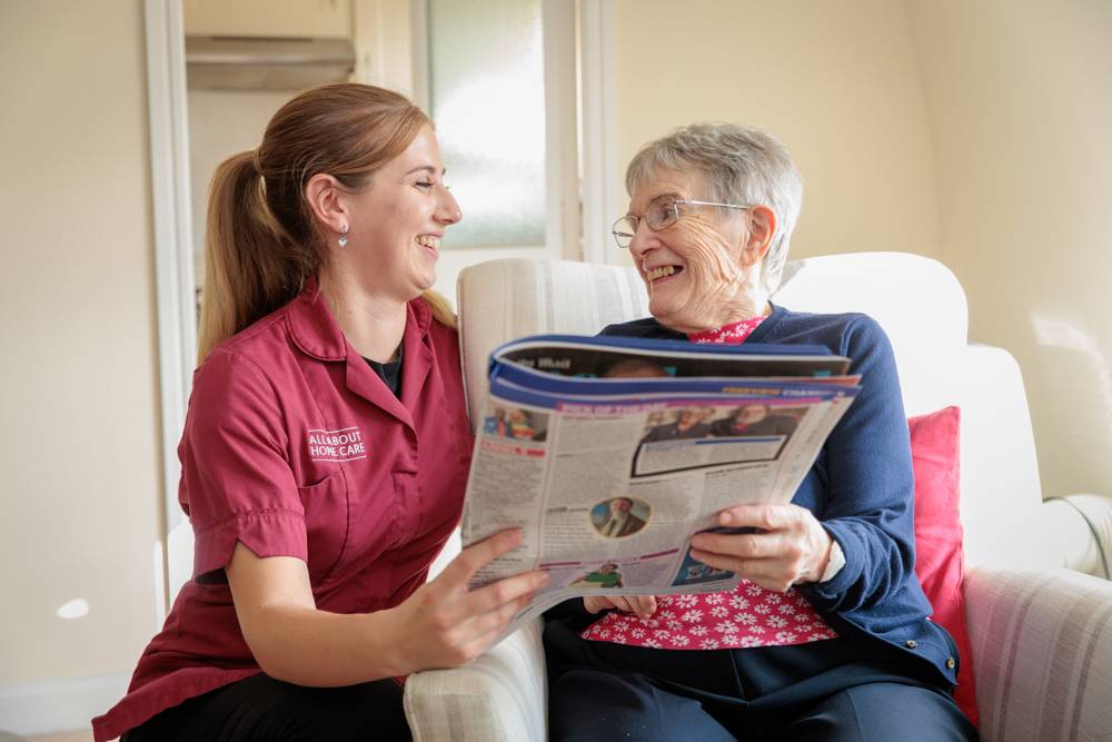 A carer and client sharing a magazine and a laugh at home