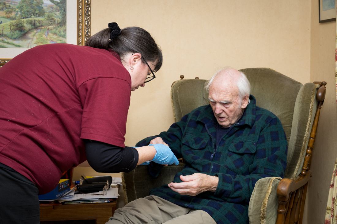 A carer checking in with a client in his armchair