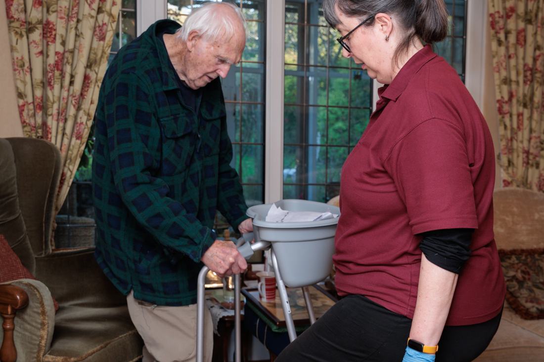 A carer supporting a client who uses a walking frame