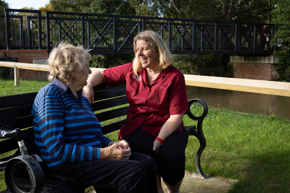 A carer and client laughing together on a park bench