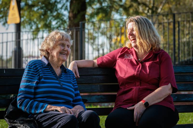 A carer and client chatting on a park bench